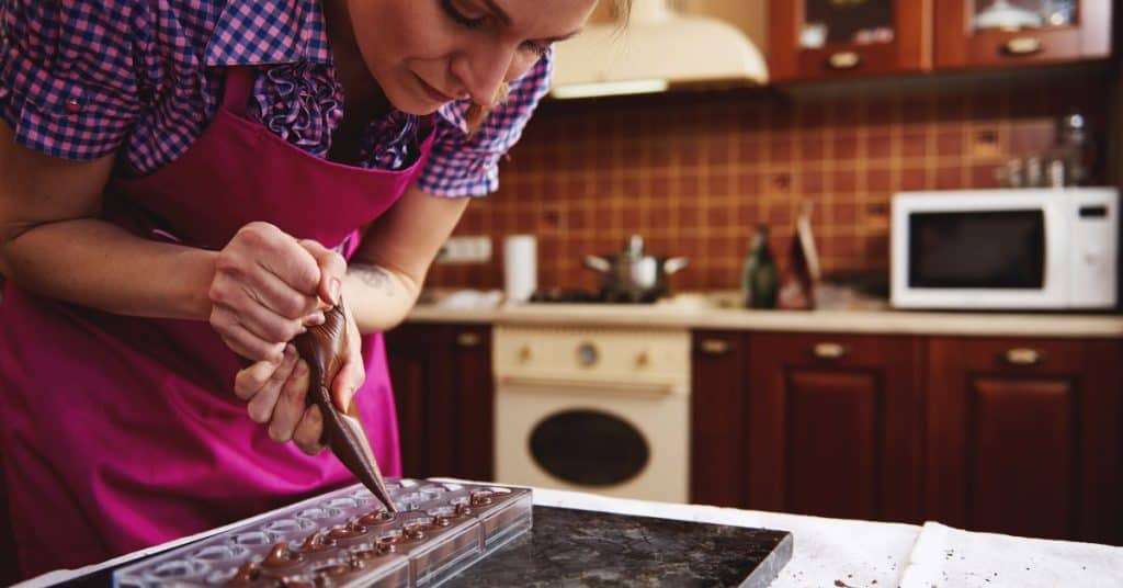  A woman looking concentrated as she pipes chocolate into a tray mold with a piping bag in her kitchen.